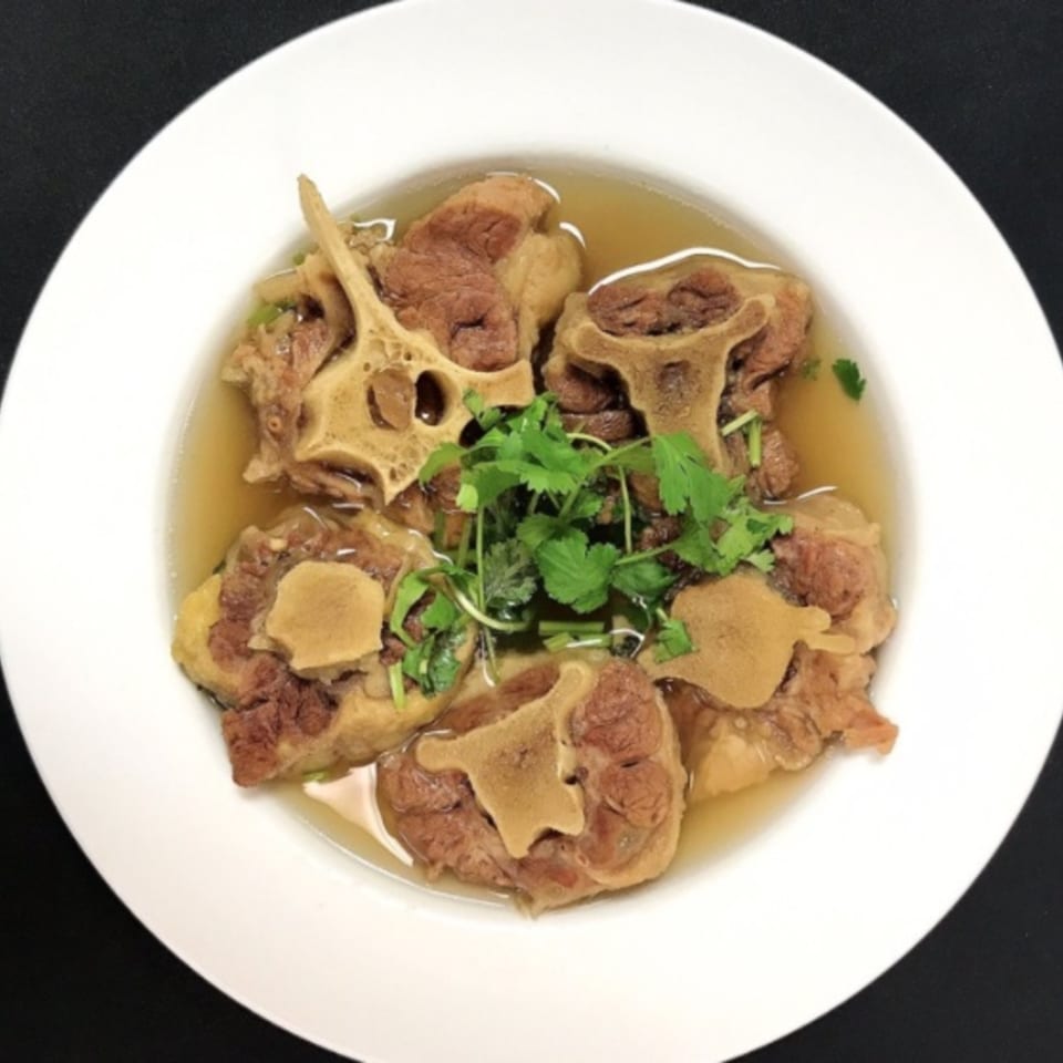 Oxtail soup with large pieces of oxtail and fresh cilantro in a white bowl.