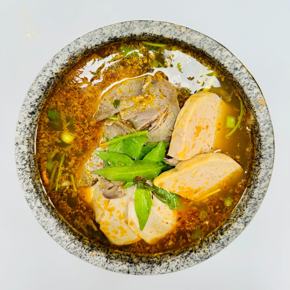 Close-up of a Vietnamese soup with beef, pork loaf, and herbs in a stone bowl.