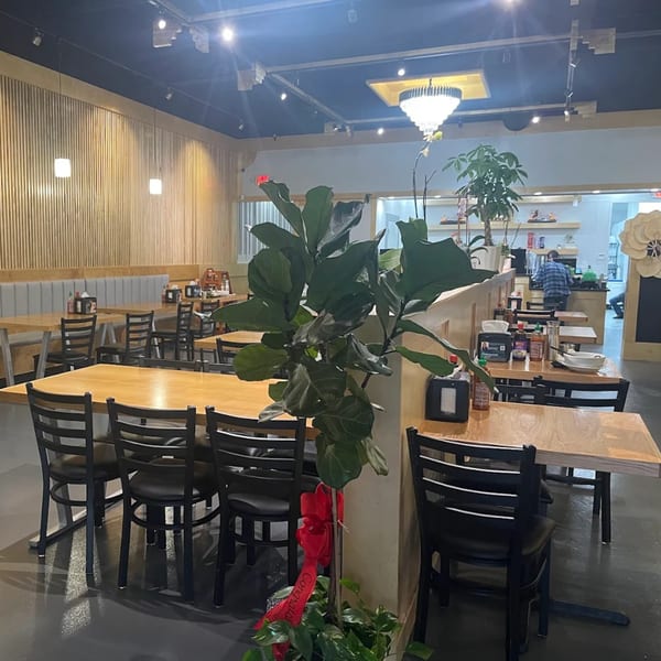 Interior of Pho House Suwanee with light wood tables, black chairs, and a large plant.