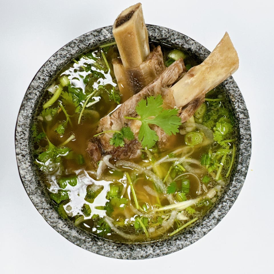 Pho House Suwanee's Vietnamese pho with large beef bones, broth, herbs, and onions in a stone bowl.