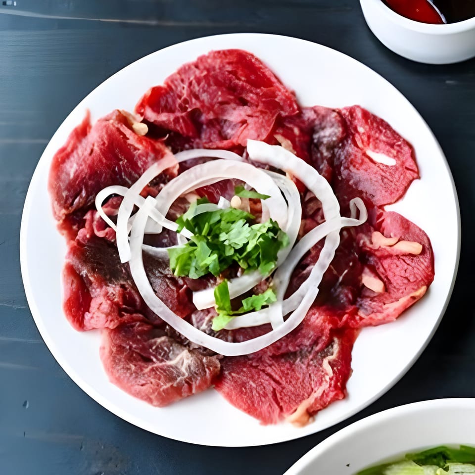 Thinly sliced raw beef, white onion rings, and fresh cilantro on a white plate.