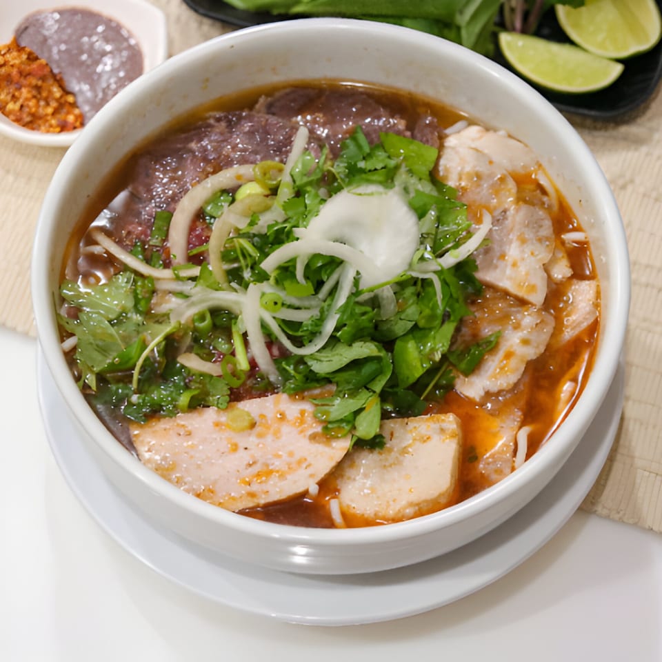 A close-up of a Vietnamese bun bo Hue soup with meat, herbs, and sliced onions.
