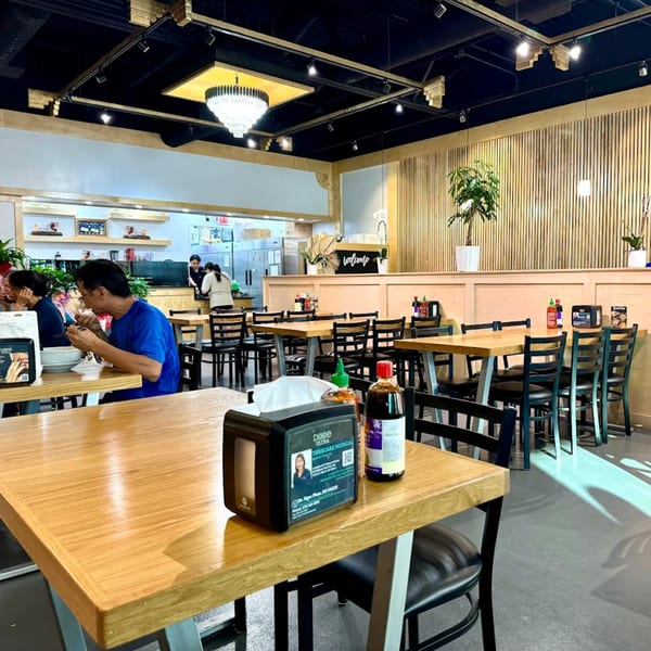 Interior of Pho House Suwanee, showing diners, wooden tables, black chairs, and a modern chandelier.